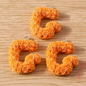 Close-up of three orange resin C-shaped charms with 3D rose textures and metal loops