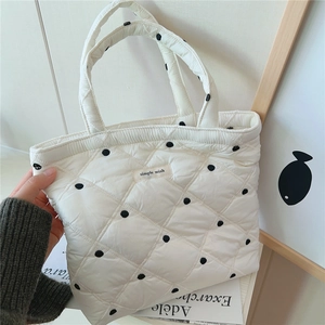 Close-up of a white quilted tote bag featuring black polka dots and a Simple Wish label
