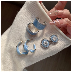 Detailed set of three light blue enamel earrings and pearls on white knit fabric