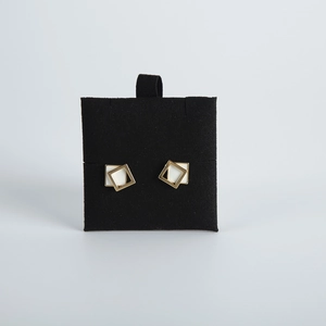 Close-up of gold geometric square earrings with white inlay on black velvet display card