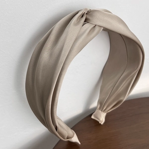 Detailed close-up of a beige twisted fabric headband with elegant satin texture