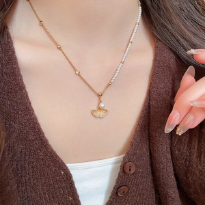Detailed view of asymmetric gold necklace with ginkgo leaf pendant and white pearls