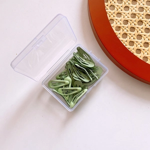 Detailed top view of green candy-colored metal hair clips in a transparent storage box