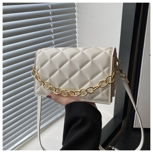 Detail of white quilted crossbody bag with golden chain accent in natural sunlight