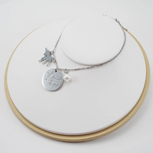 Collier licorne en argent avec perle et pendentif gravé posé sur un support blanc rond