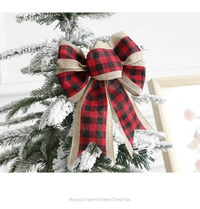 Close-up of a red and black buffalo plaid Christmas bow on a snowy evergreen tree branch