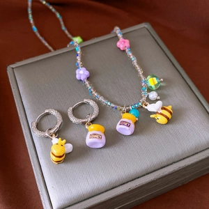 Detail of bee and honey jar pendants on a colorful beaded necklace and earrings set