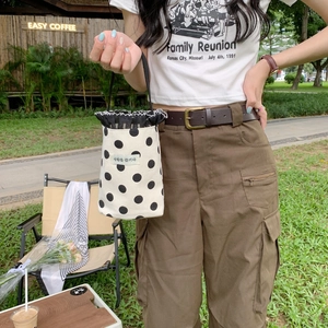 Close-up of beige polka dot canvas bag with black ruffle edge and handle in outdoor setting