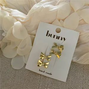 Detailed view of four golden metal bow hair clips displayed on a white product card