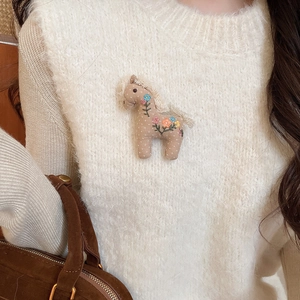 Detail showing hand-stitched horse brooch with floral embroidery on a white sweater