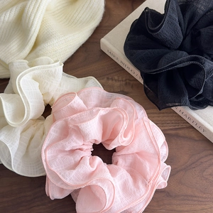 Three large oversized layered ruffle scrunchies in pink, cream, and black on wood