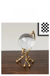 Detail of a minimalist gold metal stand holding a transparent crystal globe ornament
