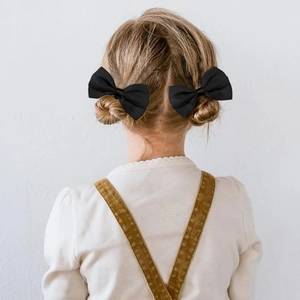 Set of 2 black ribbed fabric bow clips on a girl's buns seen from the back view