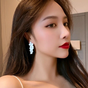 Elegant white floral drop earrings with matte finish worn by model in a soft close-up
