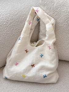 Minimalist cream tulle tote bag with colorful embroidered bows on textured fabric