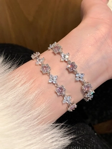 Detail of floral zircon bracelets on wrist featuring pink and white gemstones and silver plating