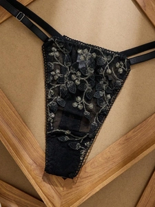 Détail d'un string en dentelle noire avec broderie florale dorée et sangles réglables