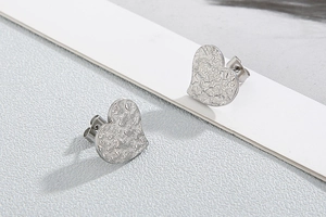 Detailed close-up of silver heart stud earrings with hammered metal texture