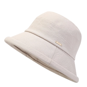 Détail d'un chapeau de soleil beige texturé avec une plaque logo métallique dorée arth