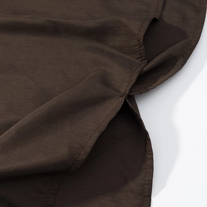 Detail view of the side slit hem and fine stitching on dark brown cotton-linen fabric