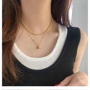 Detail of 18K gold-plated double-layer necklace with beaded chain and ball pendant on model