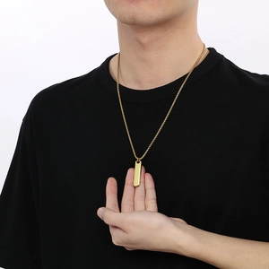 Close-up of a minimalist gold rectangle bar pendant necklace on a male model with black shirt