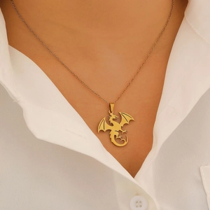 Détail d'un collier pendentif dragon doré porté par un mannequin sur chemise blanche