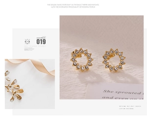 Détail de boucles d'oreilles dorées avec halo en zircone cubique sur fond en tissu texturé