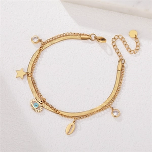 Double-layered gold chain bracelet featuring devil eye, star and shell charms on white marble