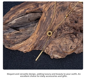 Close-up of gold titanium steel Y-shaped necklace with ring and bar pendant on bark