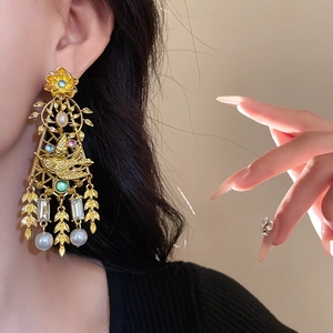 Detail of vintage gold flower bird earrings with resin pearls and tassels on model