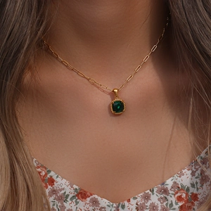 Detail of gold paperclip chain necklace featuring a square green gemstone pendant on neck