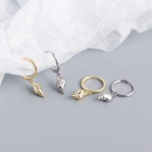 Detail of silver and gold shell charm hoop earrings on a textured paper background