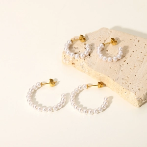 Detailed view of elegant C-shaped pearl earrings on a textured stone platform