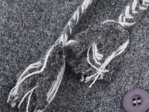 Detailed close-up of textured grey boucle fabric with round button and woven tassel rope