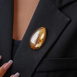 Close-up of a polished gold-tone teardrop brooch on a black blazer lapel