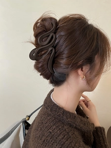 Detail view of a large matte brown shark hair claw clip on a woman's bun hairstyle