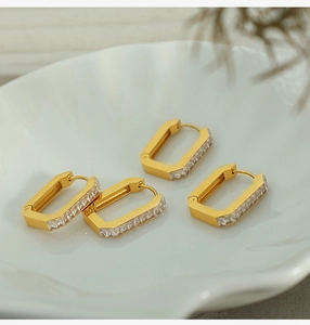 Detailed close-up of two pairs of gold rectangular hoop earrings with cubic zirconia on white plate