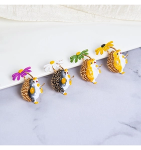 Detailed view of four cute enamel hedgehog brooches holding colorful flowers on marble