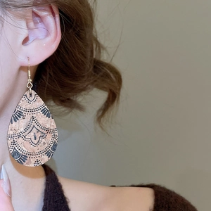 Close-up of bohemian leather teardrop earrings with black leaf pattern on a model