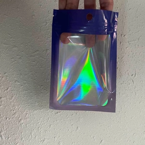 Handheld view of a holographic resealable pouch with a clear window and hanging hole