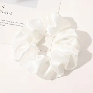 Detail view of a white satin silk scrunchie with soft folds on a minimalist background
