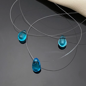 Macro shot of three teal teardrop glass pendants on an invisible fishing line chain
