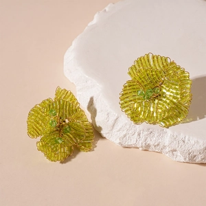 Dettaglio macro di orecchini a fiore con perle di vetro verdi e filo metallico oro