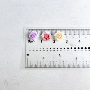 Detailed view of 1cm resin rose nail charms in purple, pink and yellow with a ruler
