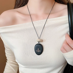 Close-up of a vintage geometric Saturn pendant on a long black cord necklace