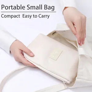 Portable travel electronics organizer bag being placed in a white canvas tote bag