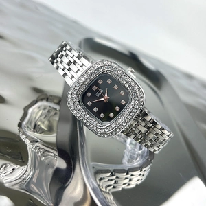 Close-up of a silver square watch with a green dial, rhinestone bezel, and metal strap