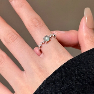 Close-up of a silver ring with a pale green gemstone and side zircon accents
