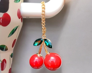 Detail of red cherry charm pendant with green rhinestones hanging on a white ceramic cup